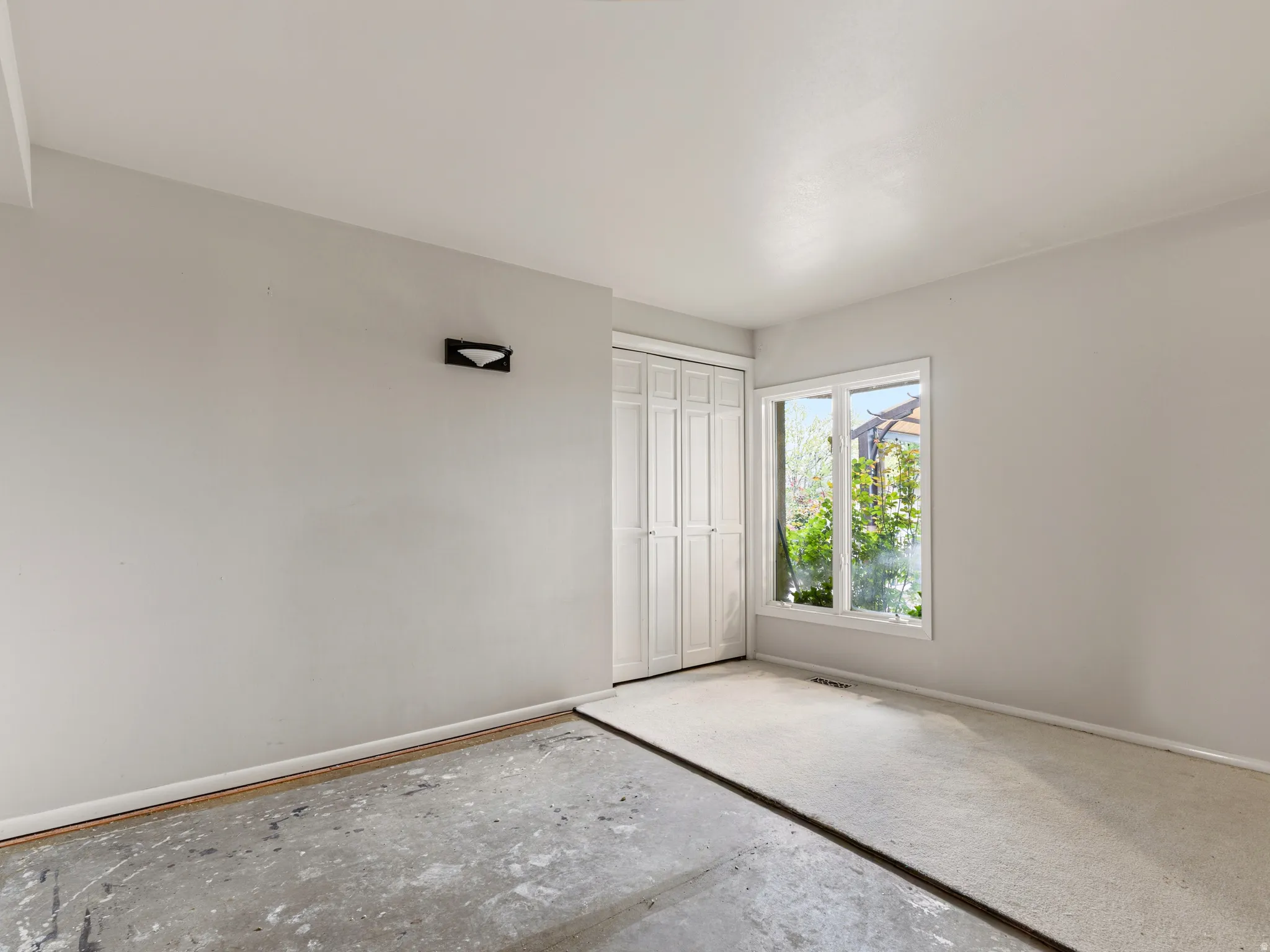Room featuring a white-framed window, white walls, and a combination of concrete and partial carpeting