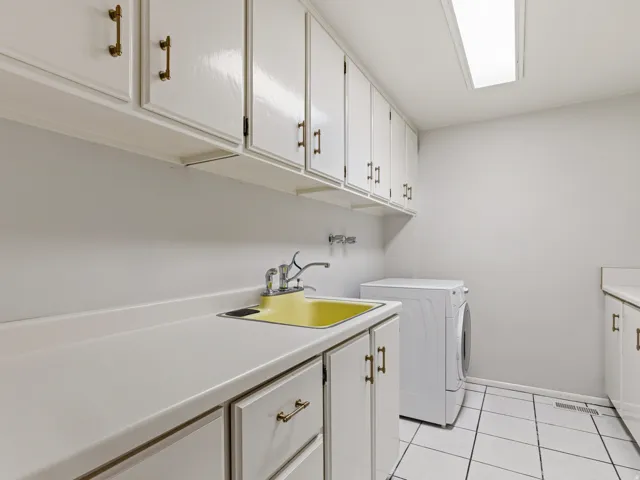 Utility area featuring white cabinetry with brass-toned hardware, extensive countertop space, a yellow utility sink with faucet, and white tiled flooring
