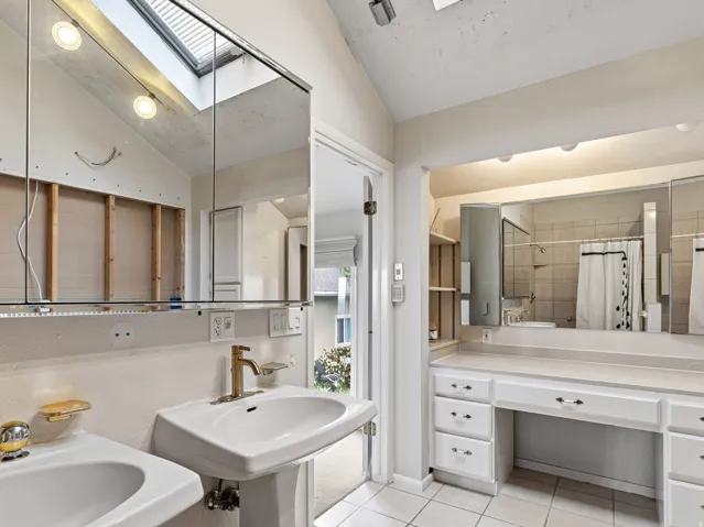 Bathroom featuring a skylight, dual pedestal sinks, a vanity area with built-in cabinetry, and tile flooring