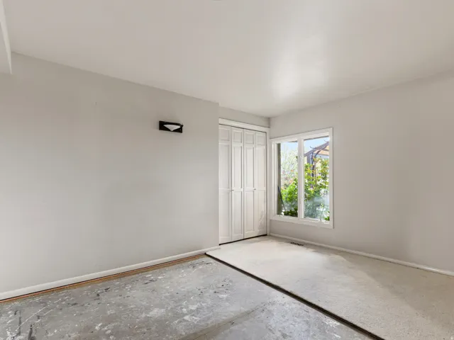 Room featuring a white-framed window, white walls, and a combination of concrete and partial carpeting