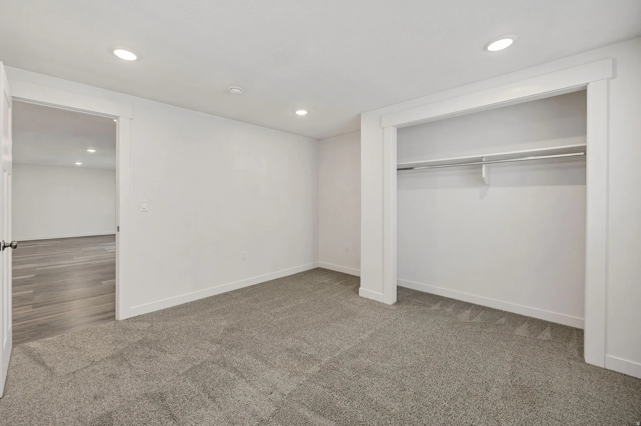 Recessed lighting, light gray carpeting, and white trim accents a spacious room