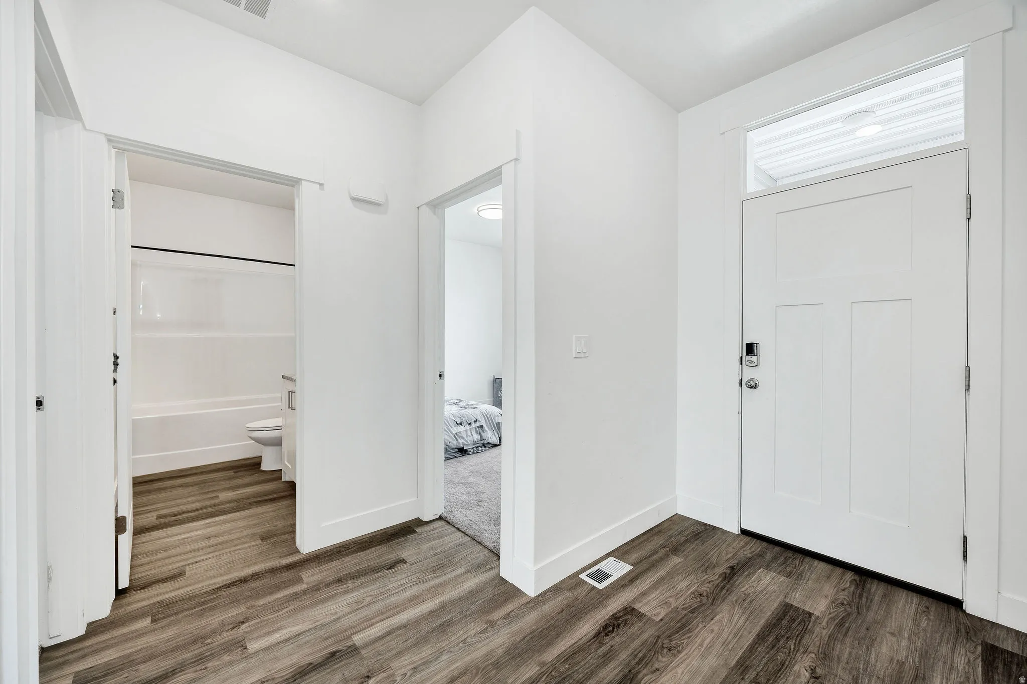 Entryway featuring plank wood-finish flooring, a white paneled front door with a transom window, and a smart lock