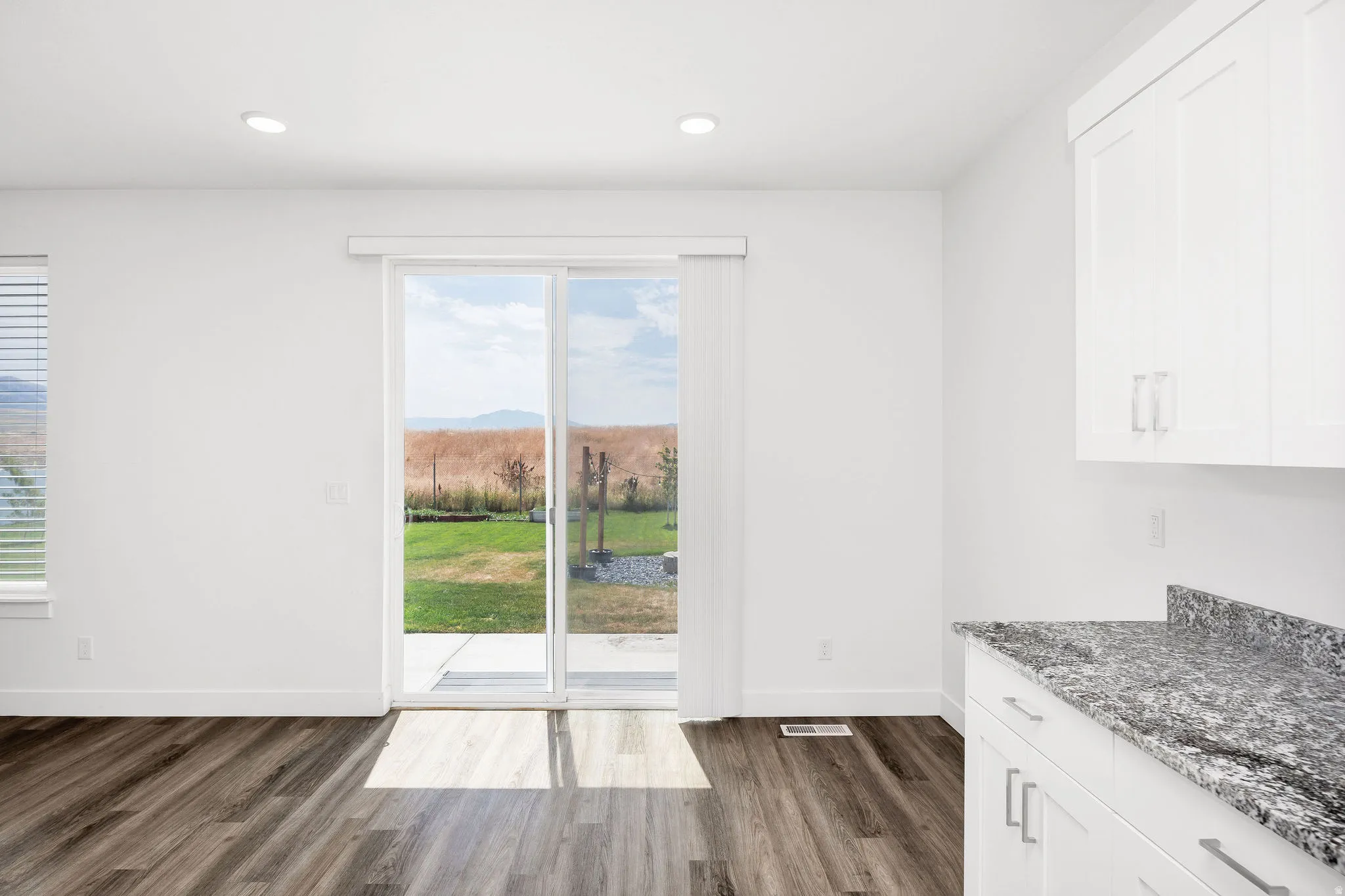 Bright interior featuring wood-finish flooring, recessed lighting, and a sliding glass door opening to a paved patio and grassy yard area