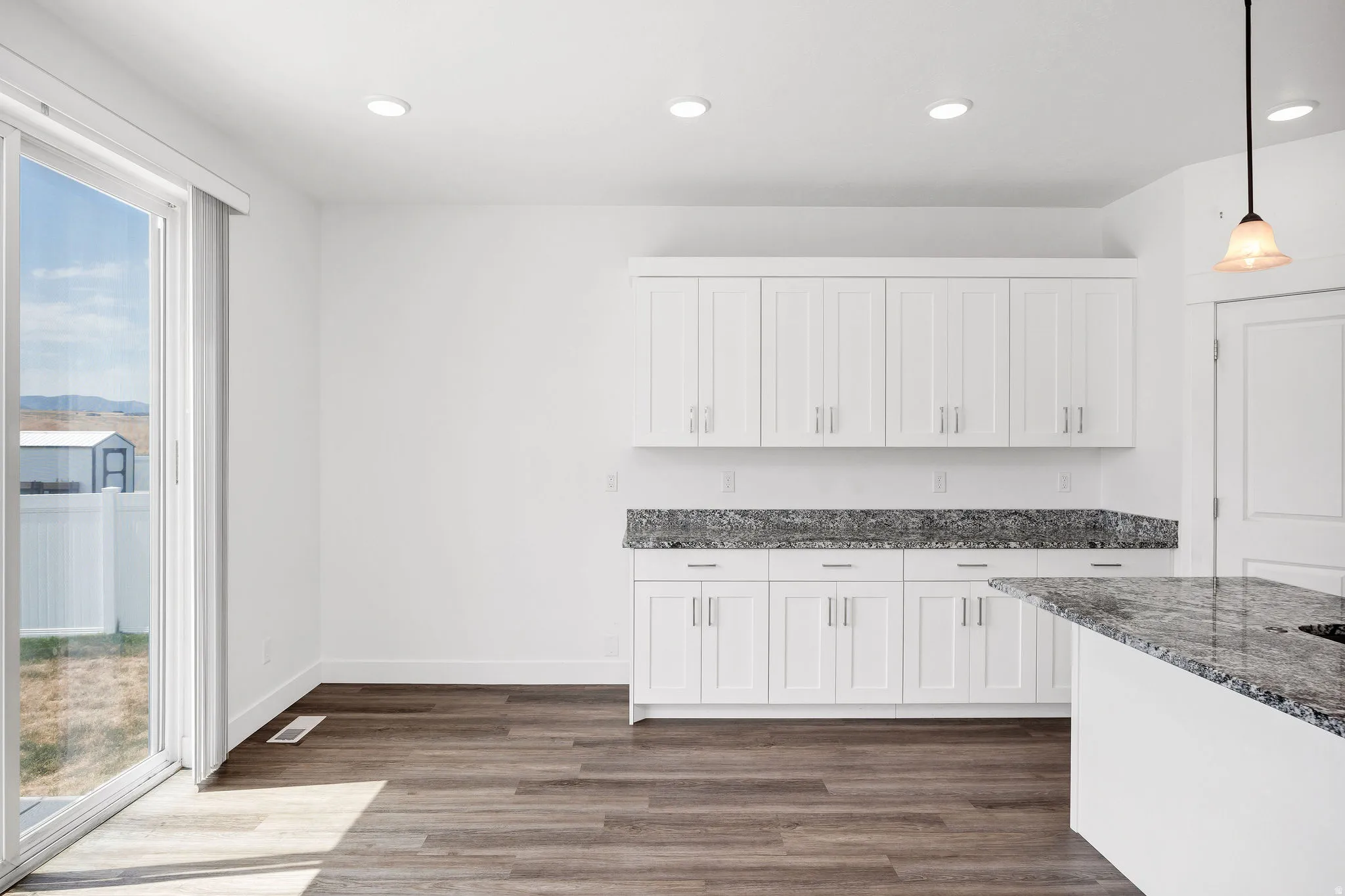 Contemporary kitchen featuring white cabinetry, dark speckled countertops, recessed lighting, and wood-finish flooring