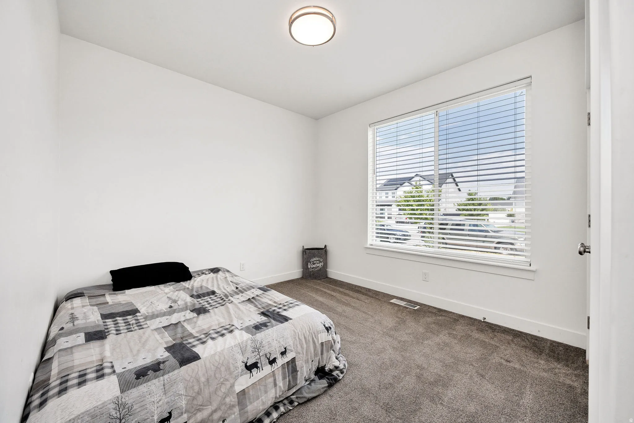 Bright room featuring a large window with horizontal blinds, neutral carpet flooring, and white baseboards