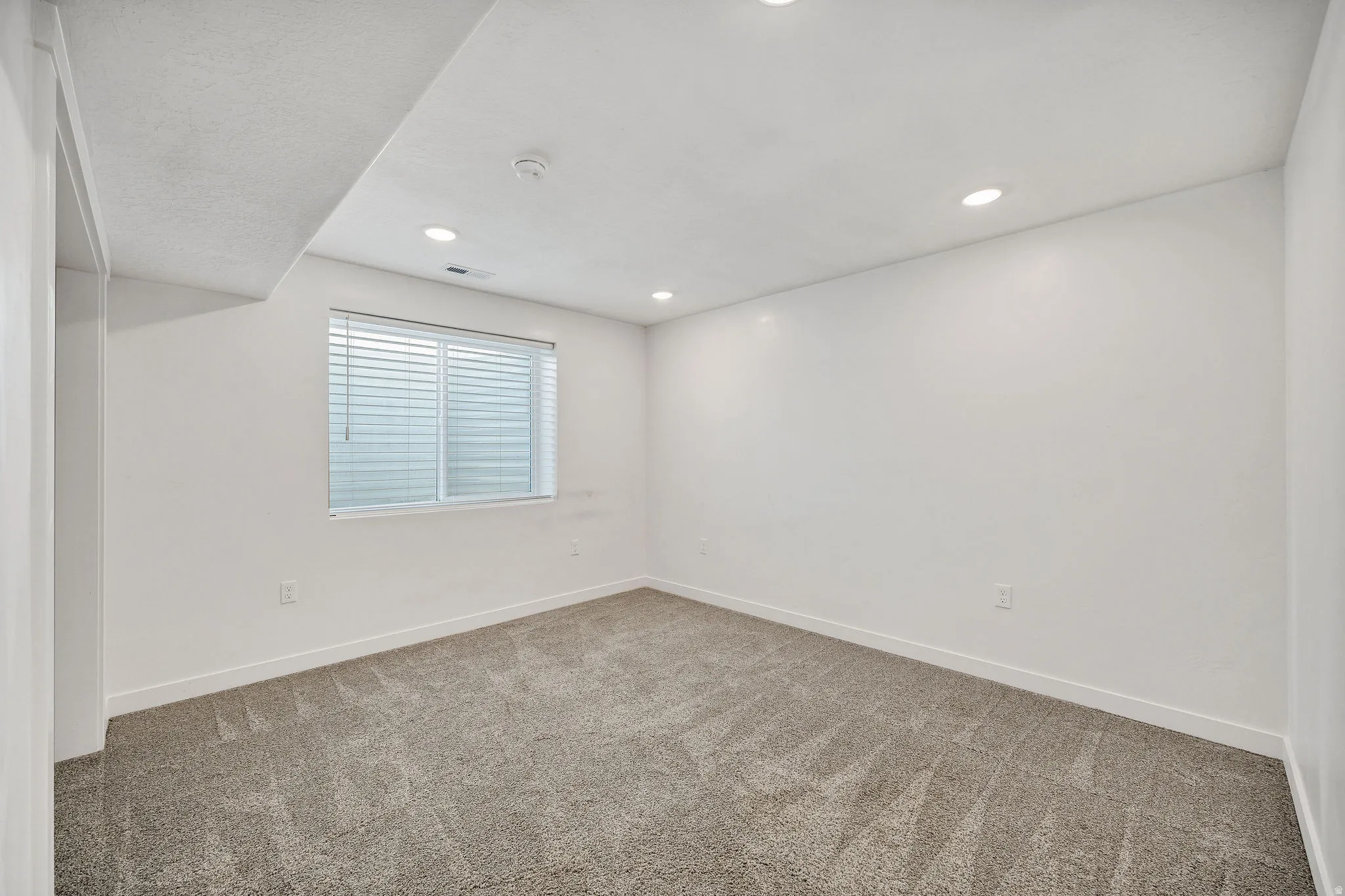 Room featuring neutral carpeting, a single window with blinds, recessed lighting, and white walls