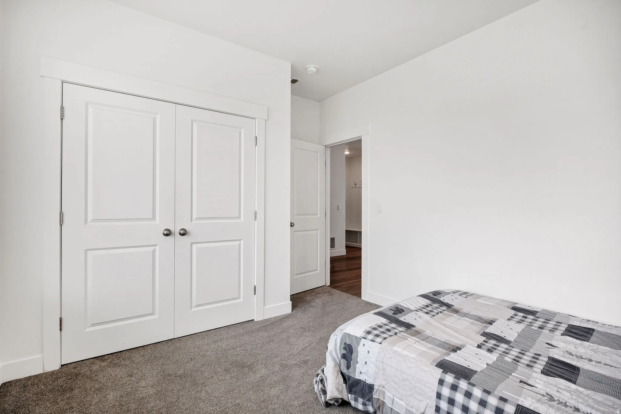 Bedroom featuring bright white walls, a double-door closet with paneling and brushed nickel hardware, and gray carpeting