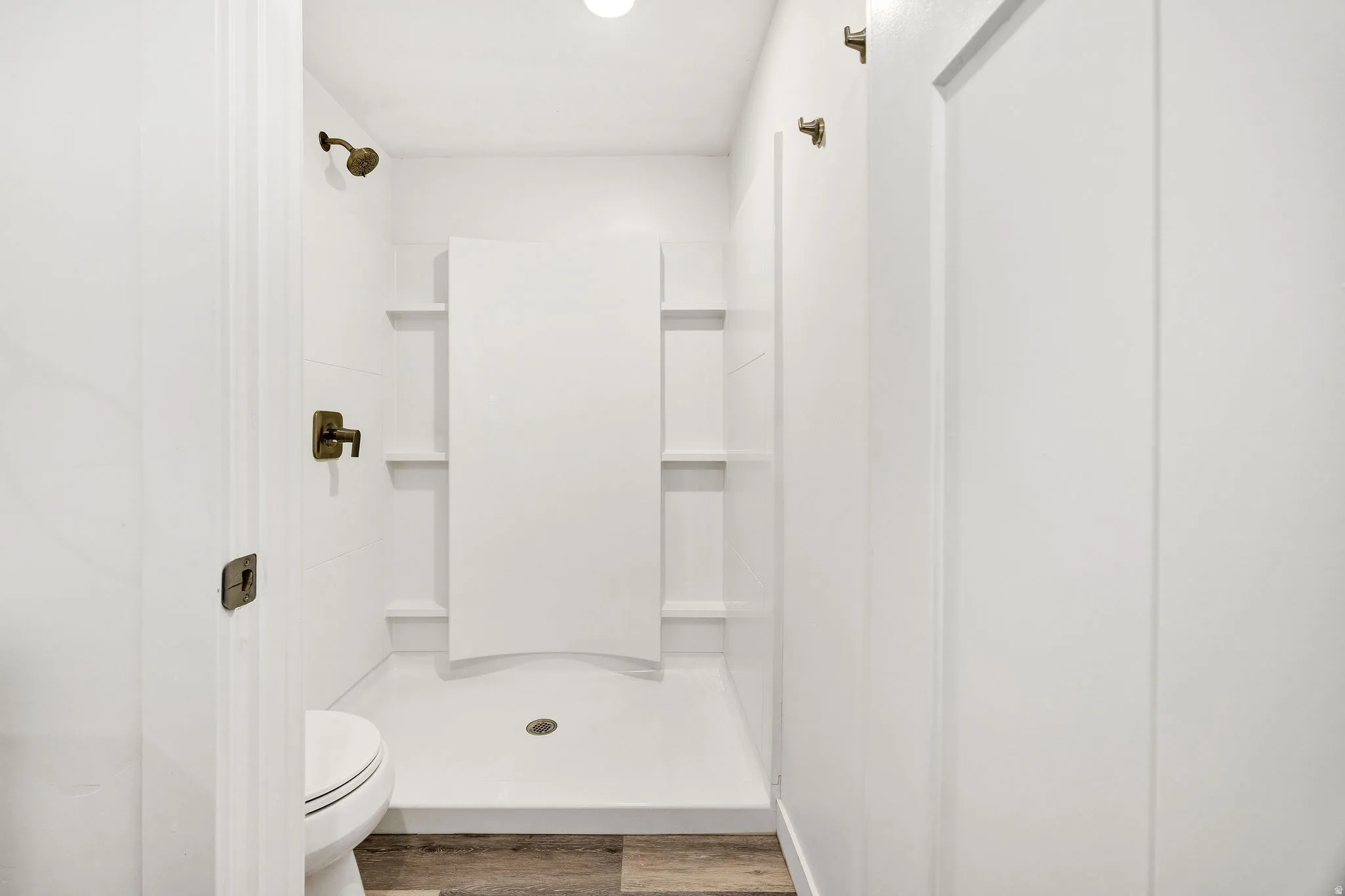Shower stall with integrated shelving, bronze fixtures, and a white toilet