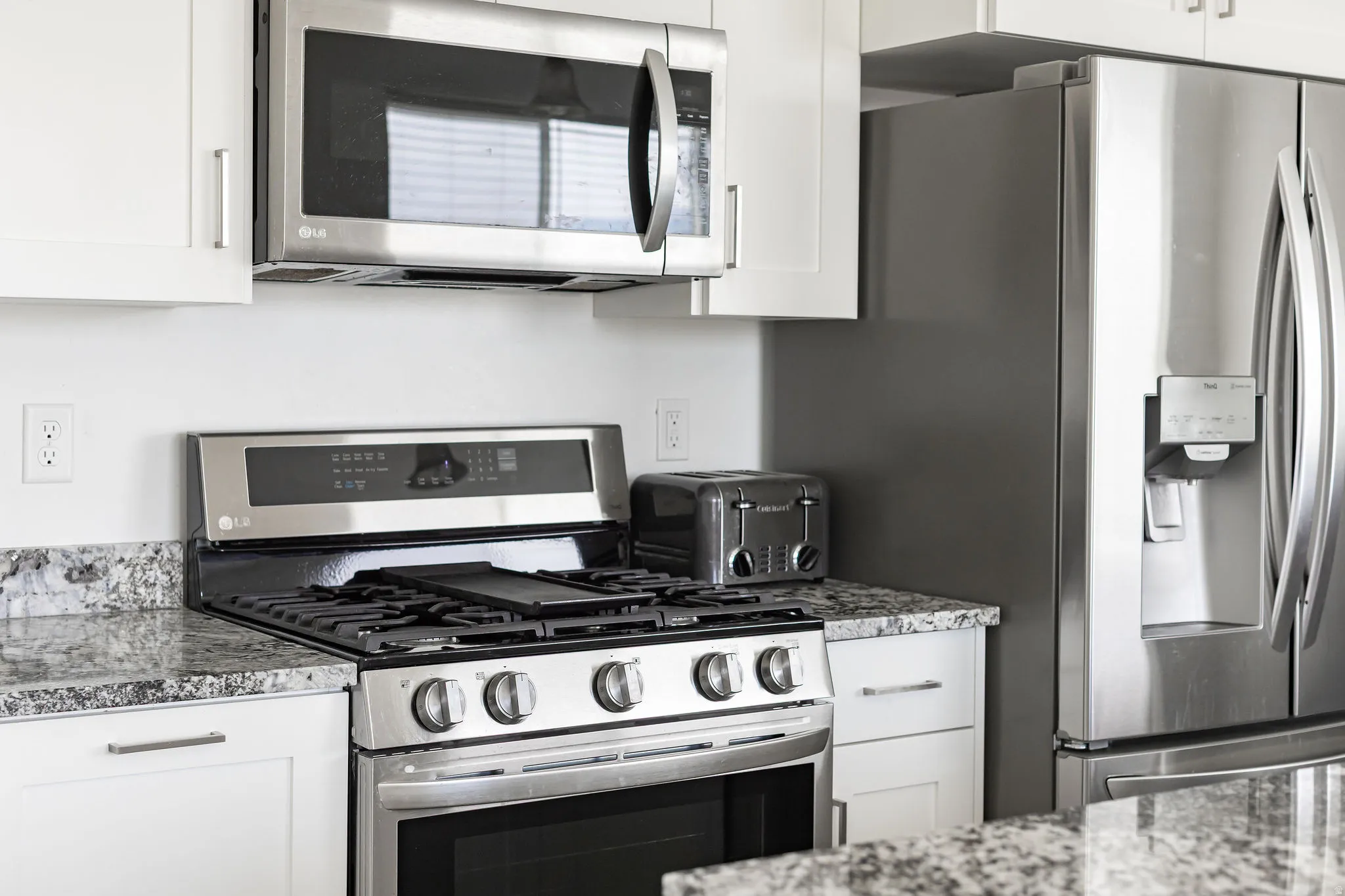 Modern kitchen featuring stainless steel appliances, white cabinetry, speckled countertops, and a gas range with an overhead microwave
