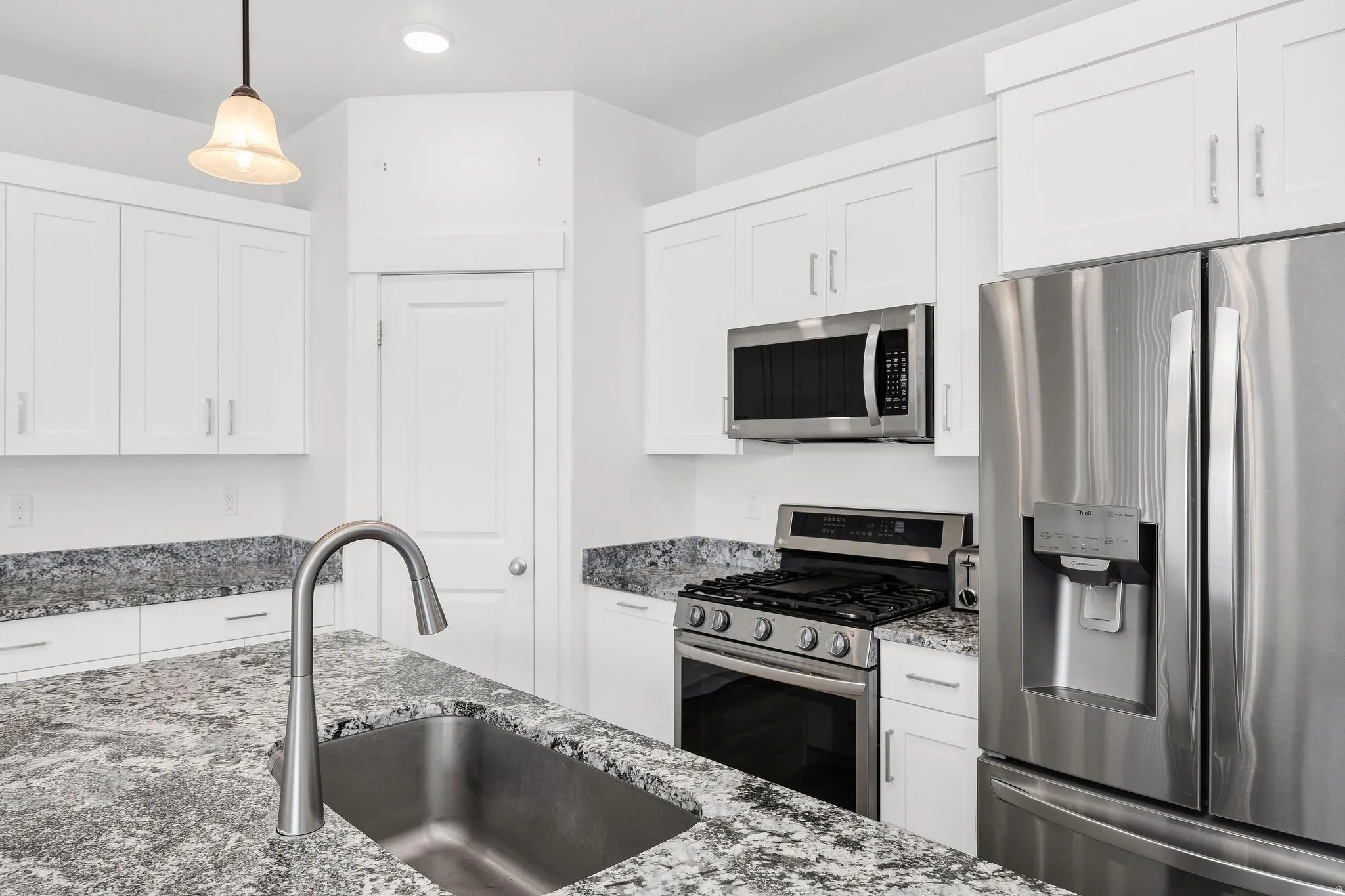 Modern kitchen featuring white shaker cabinetry, stainless steel appliances, speckled stone countertops, a single-basin sink with a gooseneck faucet, and recessed lighting