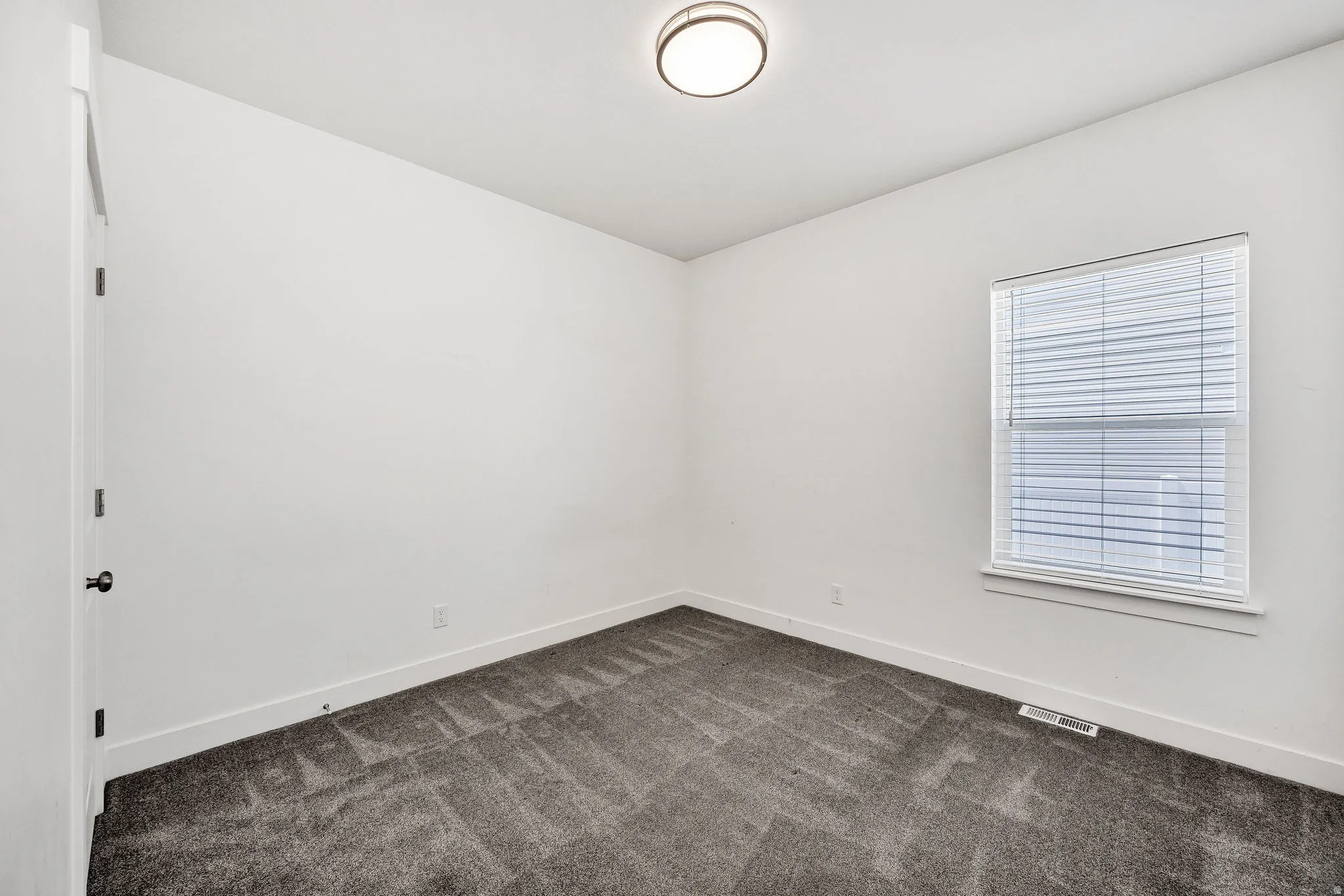 Room featuring grey patterned carpeting, white walls, and a single window with horizontal blinds