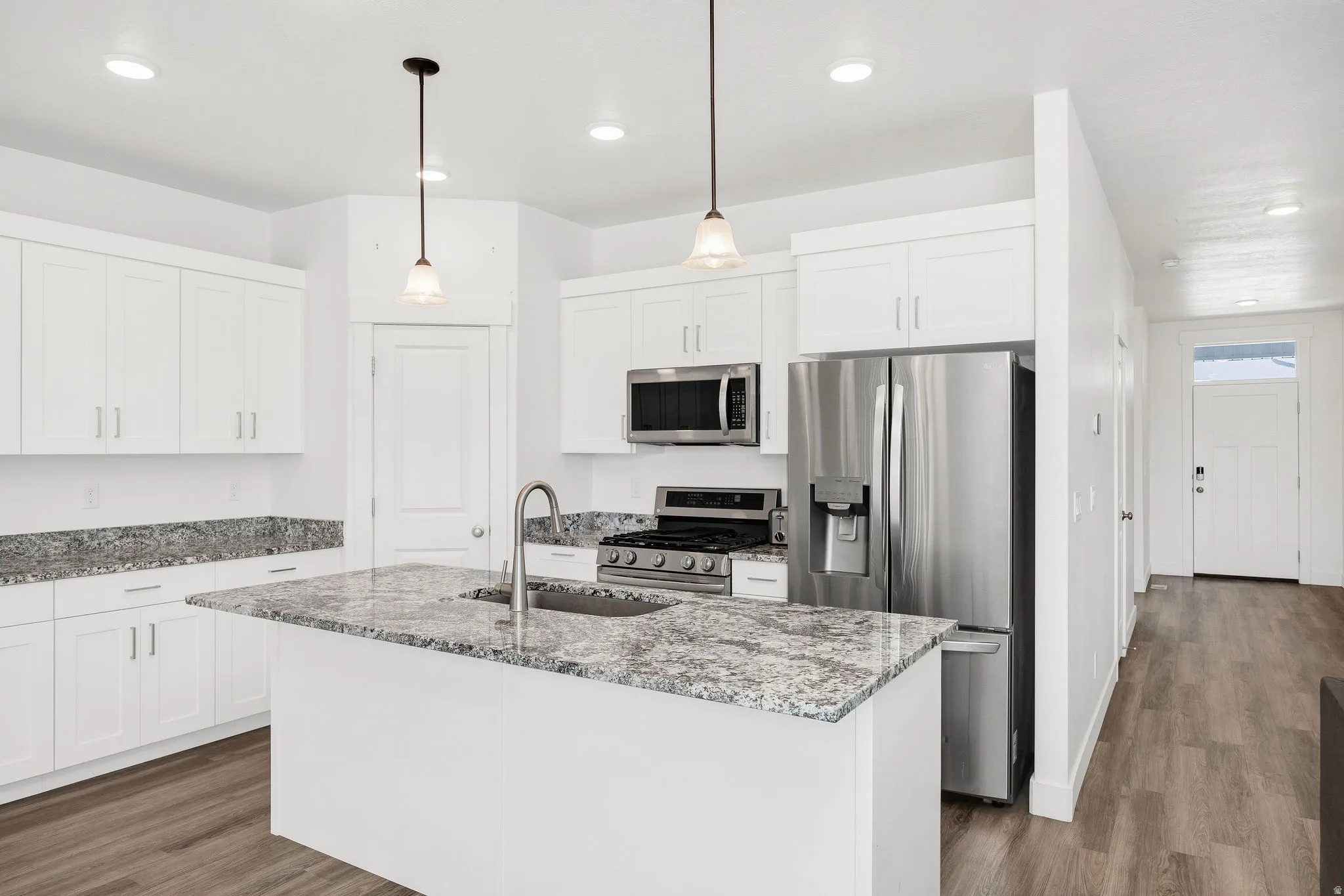 Modern kitchen featuring a central island with a sink, white shaker cabinetry, stainless steel appliances, and granite countertops