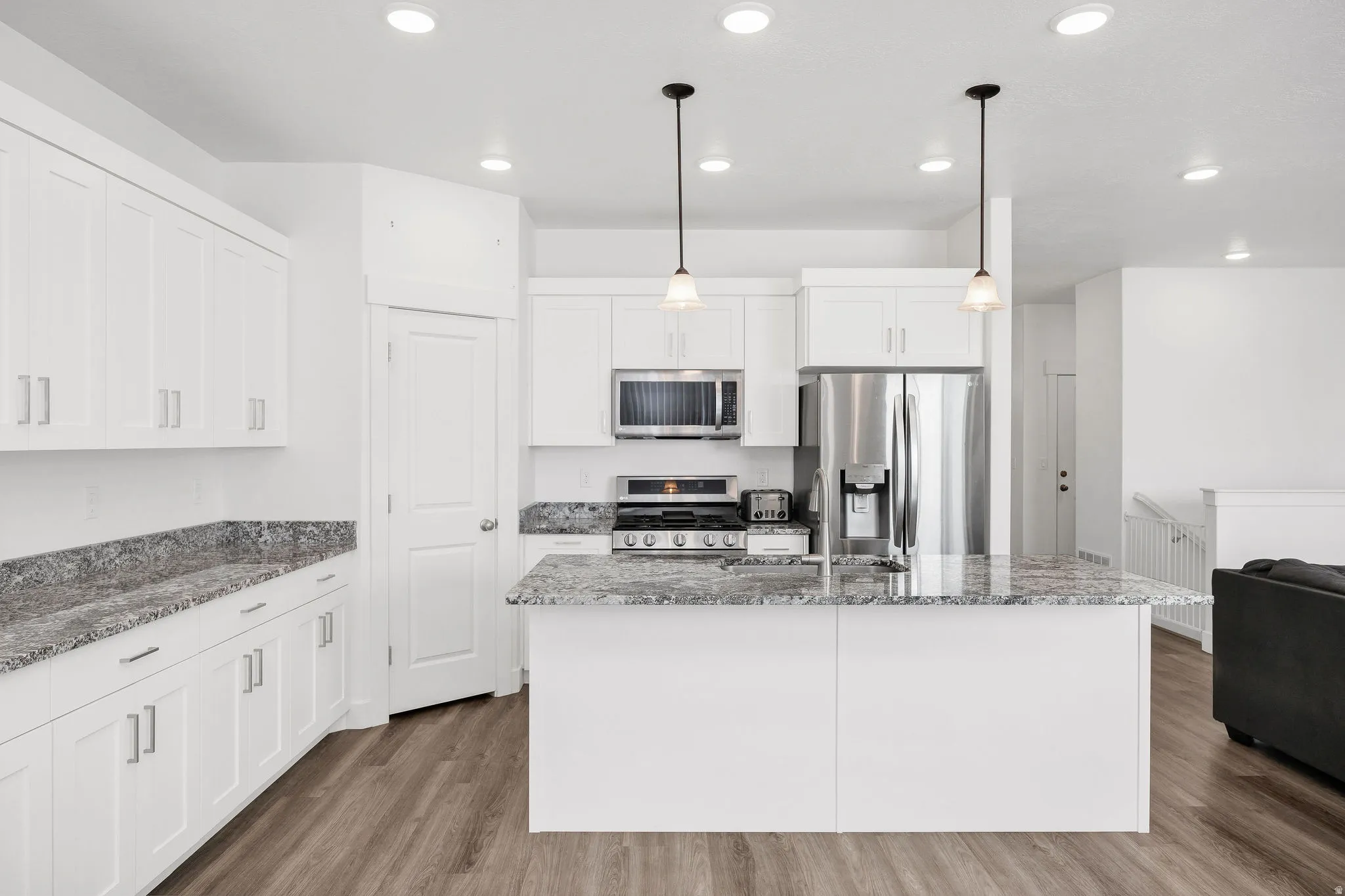 Kitchen featuring white shaker-style cabinetry, stainless steel appliances, speckled stone countertops, and wood-finish flooring