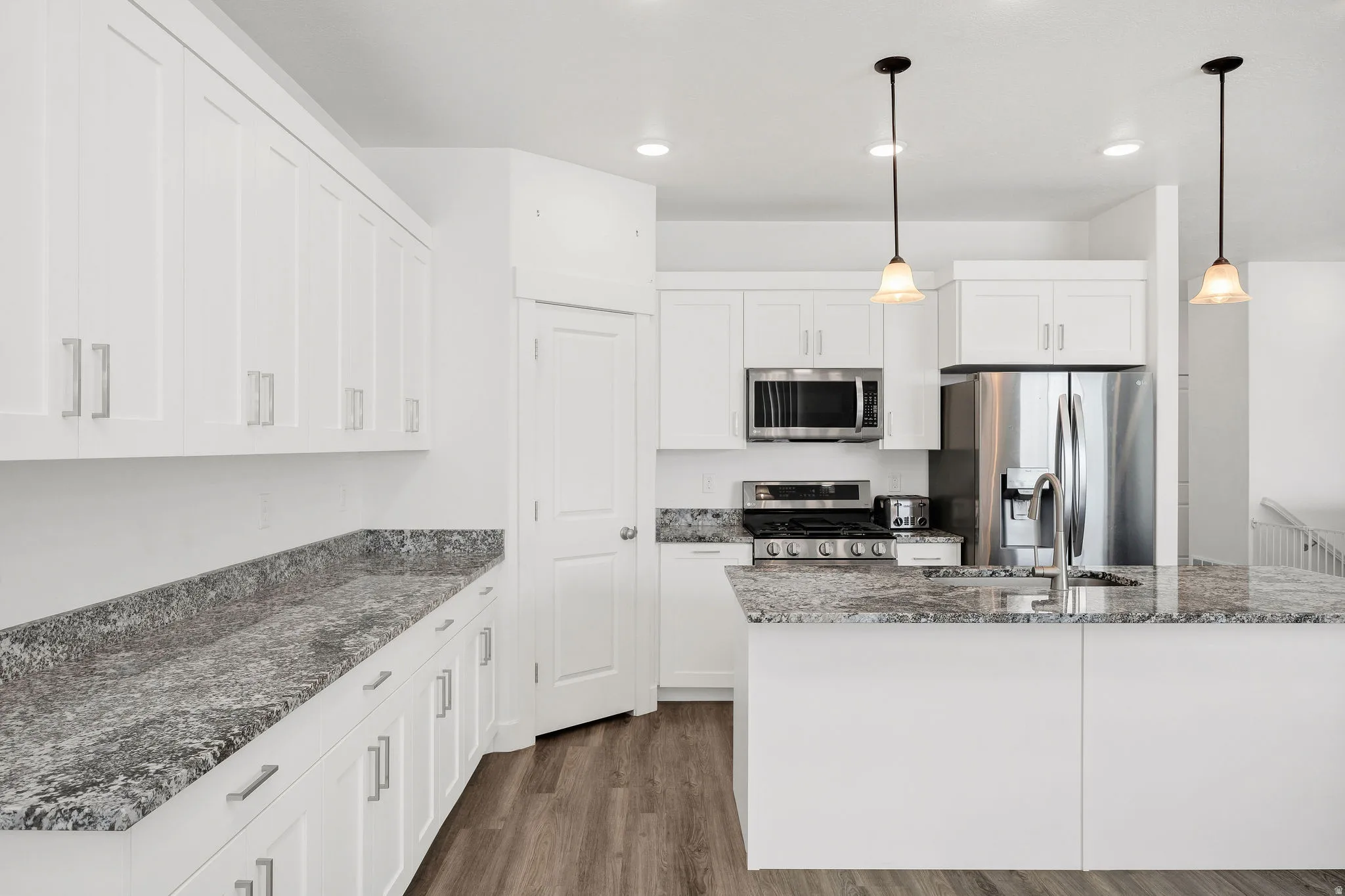 Open-concept kitchen featuring white cabinetry, stainless steel appliances, granite-style countertops, wood-finish flooring, and pendant lighting over the island