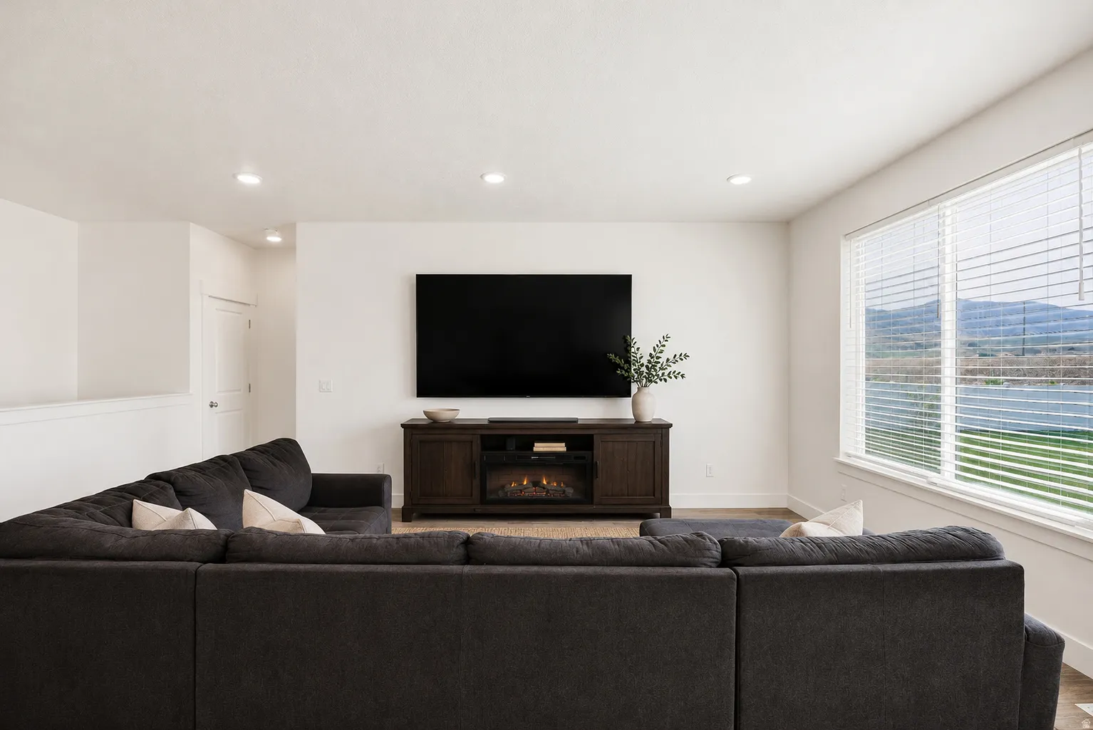 Bright living space featuring a large window with horizontal blinds, recessed lighting, and wood-finish flooring
