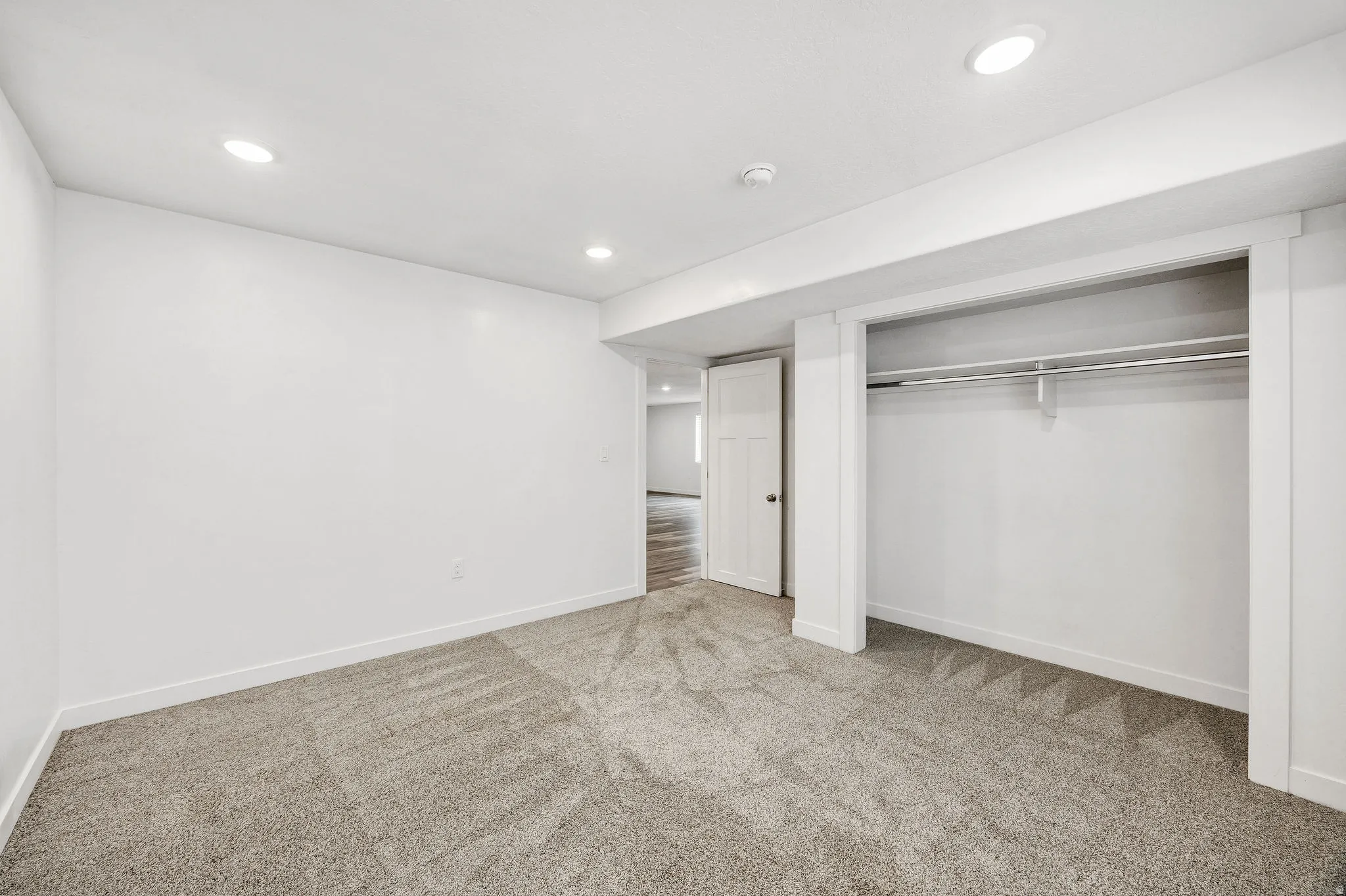 Carpeted room with a built-in closet featuring a clothes rod, recessed lighting, and white baseboards
