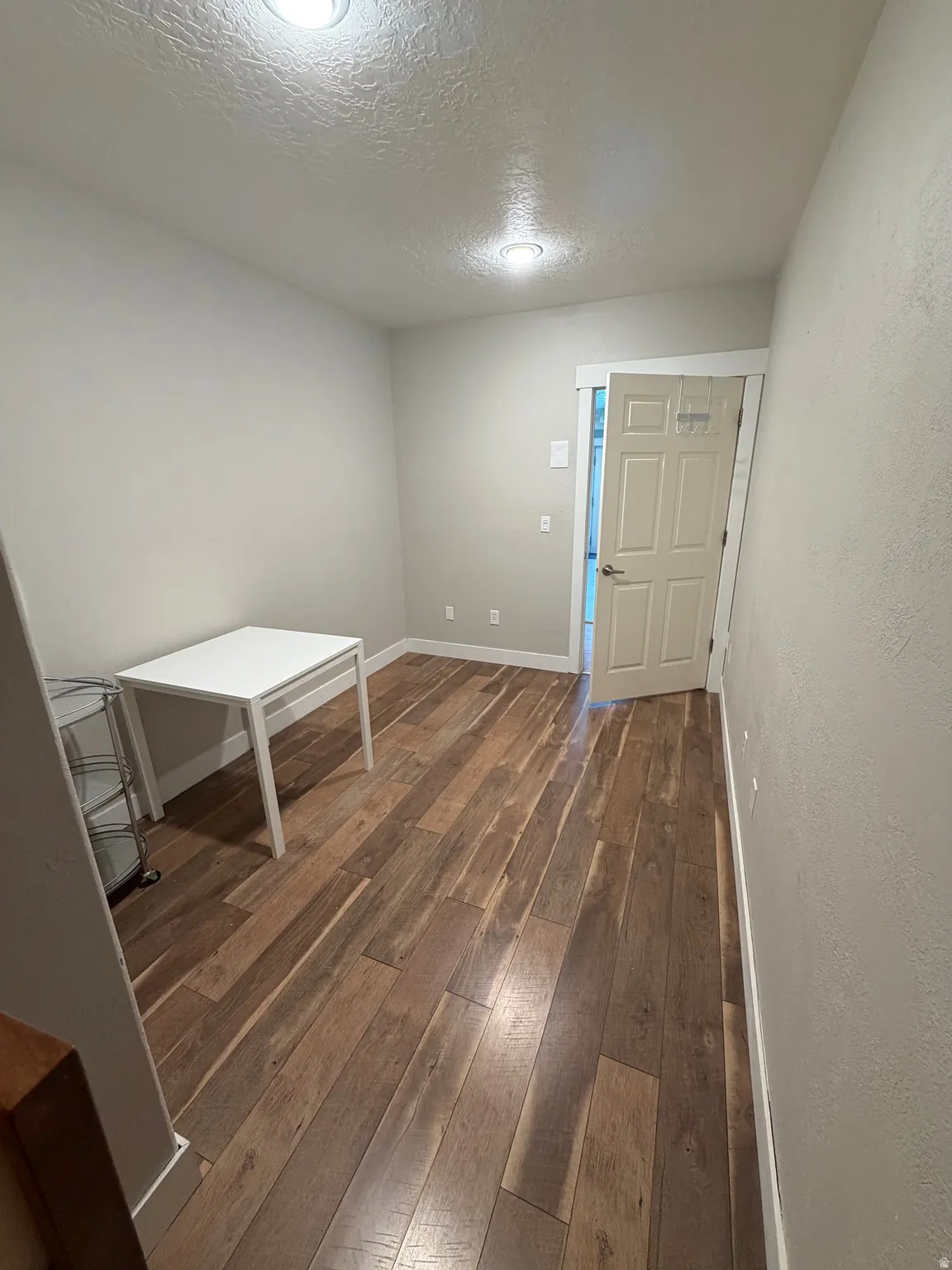 Wood-finish flooring throughout, featuring recessed lighting, light gray wall paint, white baseboards, and a white interior door with a chrome handle