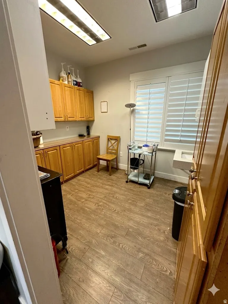 Spacious room featuring extensive wood cabinetry with metal hardware, wood-finish flooring, and white plantation shutters