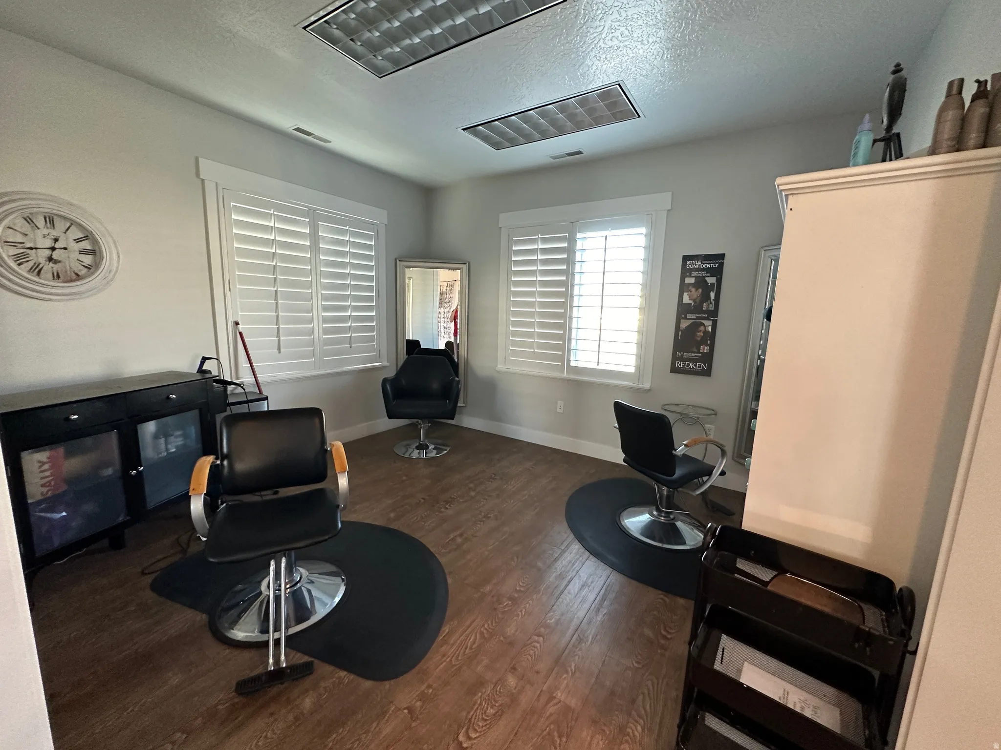 Bright interior space featuring wood-finish flooring, two large windows with white plantation shutters, and recessed ceiling lighting