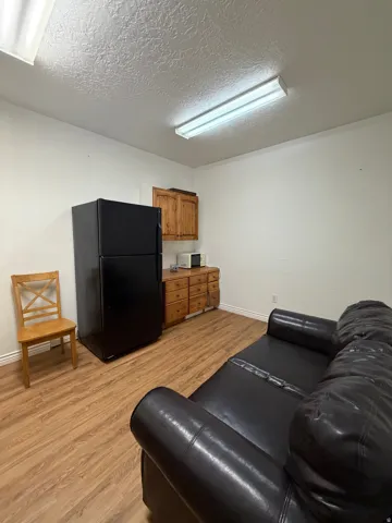 Compact kitchenette area featuring wood-finish cabinetry and flooring, paired with overhead fluorescent lighting