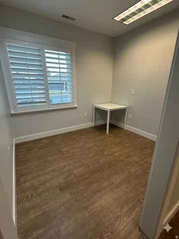Room featuring wood-finish flooring, plantation shutters, and recessed fluorescent lighting