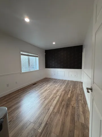 Spacious room featuring wood-finish flooring, recessed lighting, and wainscoting details