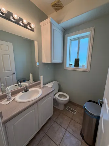 Bathroom featuring a single vanity with an integrated sink, a rectangular mirror, overhead vanity lighting, a window with white trim, and tile flooring