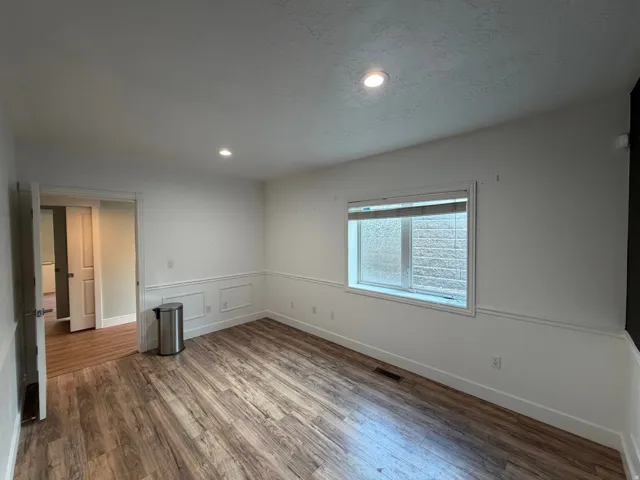 Spacious interior room featuring wood-finish flooring, recessed lighting, and wainscoting