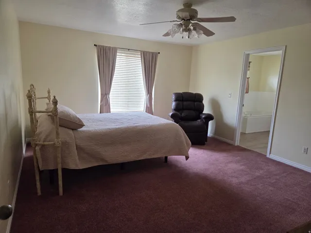Spacious room featuring neutral wall tones, a ceiling fan with light fixture, and an open doorway revealing an adjacent area with a white built-in tub