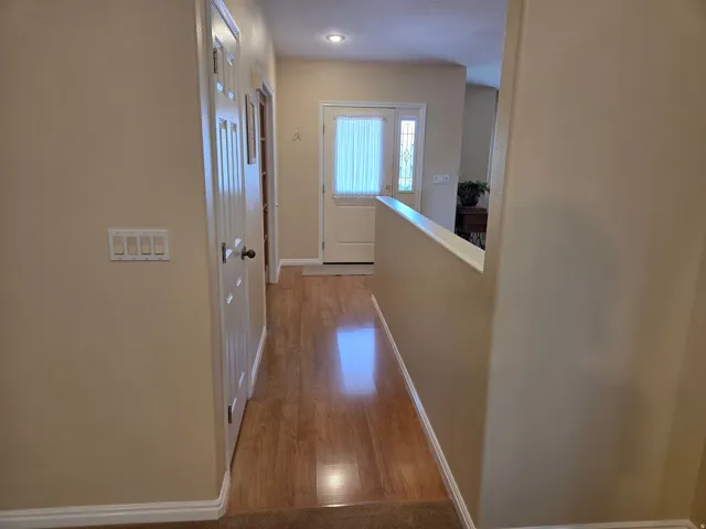 Hallway featuring wood-finish flooring, light tan wall paint, and white baseboards