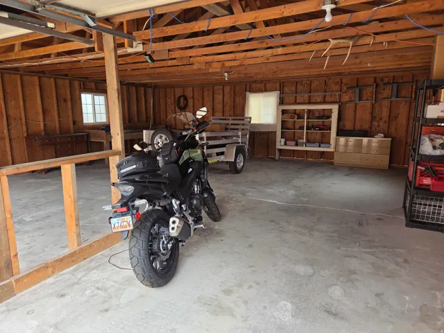 Spacious garage featuring exposed beam ceiling, concrete flooring, wood paneling, and a transom window