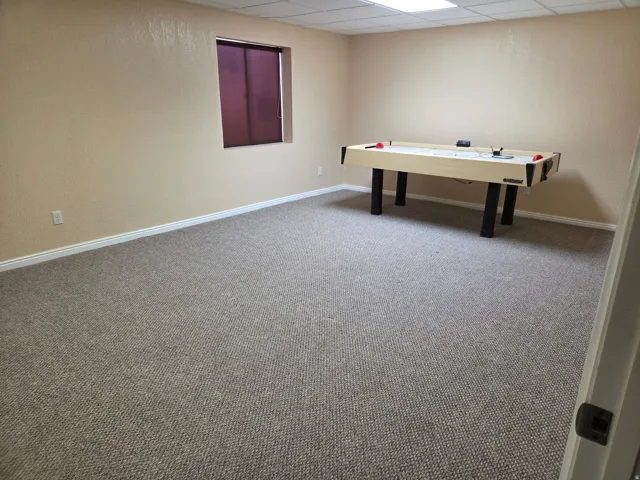 Carpeted room featuring a window with purple blinds, textured walls, and white baseboards