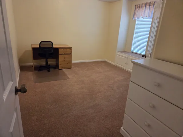 Carpeted room featuring a built-in window seat with cabinet storage, a window with blinds, and light-toned walls