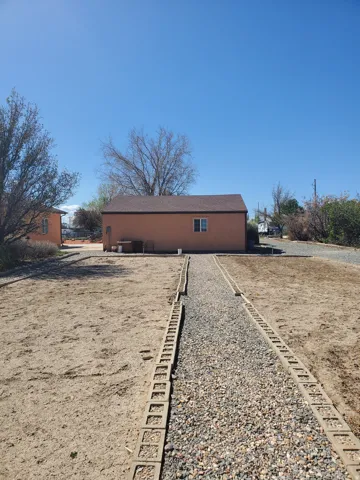Rear exterior of the structure featuring an earth-toned stucco finish and a brown shingle roof