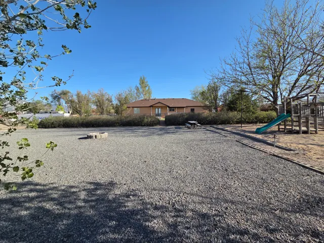 Expansive gravel yard featuring a fire pit, mature trees, and a picnic area
