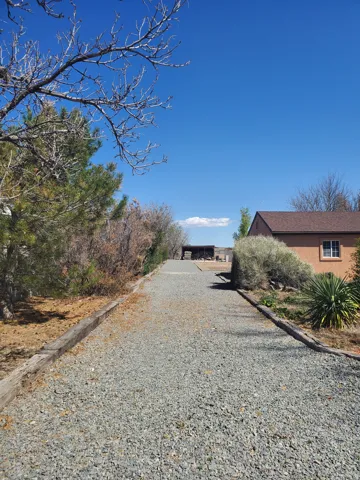 Gravel driveway leading to a stucco-exterior structure with a brown shingle roof and a single window