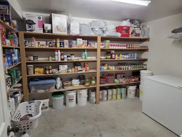 Dedicated storage room featuring extensive built-in shelving, concrete flooring, and a chest freezer