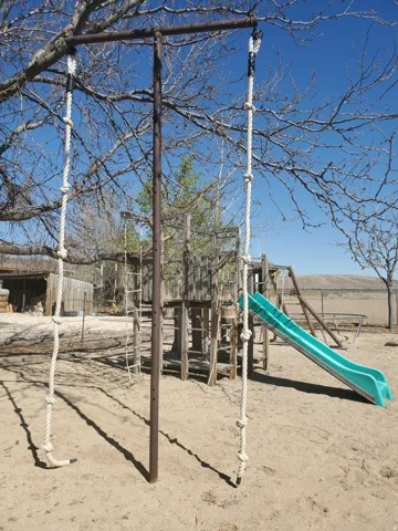 Outdoor play area featuring a wooden structure with a green slide and two rope climbs suspended from a metal frame