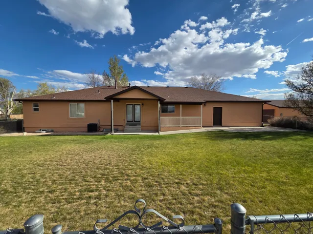 Expansive rear yard featuring a large concrete patio, covered porch area with railing, and stucco exterior