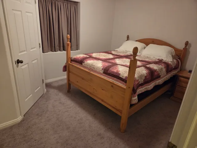 Bedroom featuring a window with privacy drapes, neutral-toned wall paint, white trim, and light-colored carpet flooring