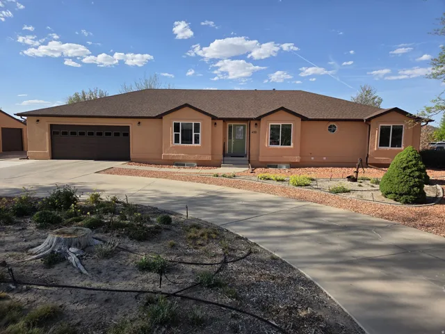 Stucco exterior with a brown asphalt shingle roof, featuring a two-car garage with a brown panel door, a concrete driveway, and landscaped rock beds