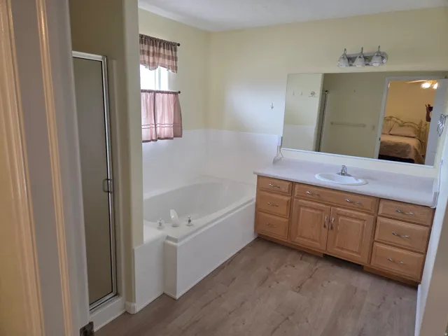 Bathroom featuring a built-in tub, a glass-enclosed shower, a single vanity with wood-finish cabinetry, a large mirror, and wood-finish flooring