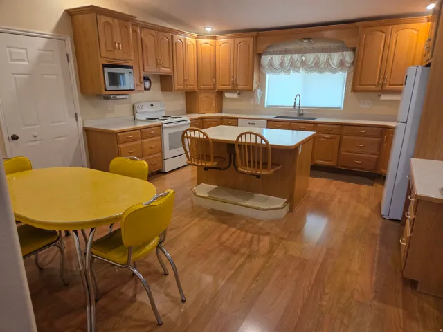 Spacious kitchen featuring extensive wood cabinetry, wood-finish flooring, white appliances, and a central island with integrated seating