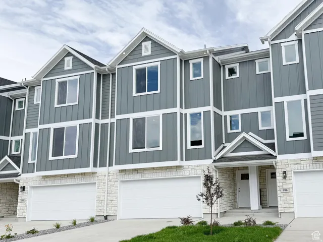 Exterior featuring gray board and batten siding, white stone veneer accents, multiple large windows, a covered entry, and an attached two-car garage