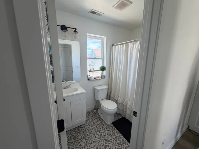 White vanity with a single basin sink, wall-mounted light fixture, and patterned floor tile