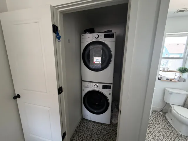 Dedicated laundry closet featuring a stacked white washer and dryer unit, set on patterned floor tiles