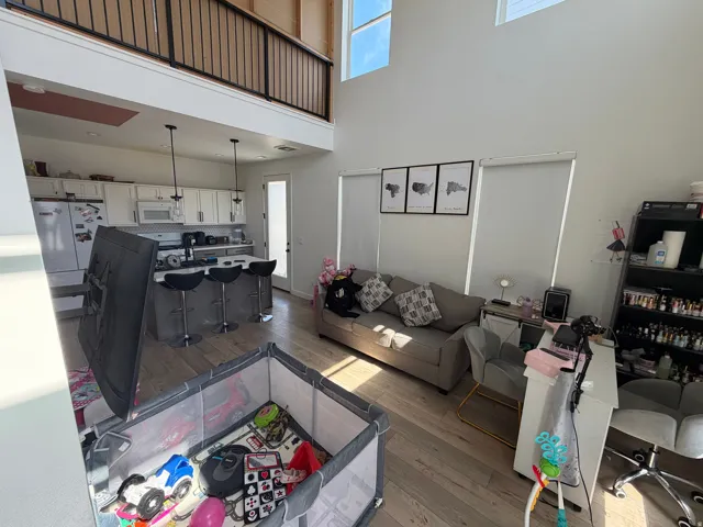 Open concept living area featuring wood-finish flooring, a kitchen island with pendant lighting, white cabinetry, and high ceilings with upper windows