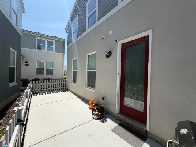 Concrete patio area featuring a red glass-paneled door, stucco exterior, and white picket fencing