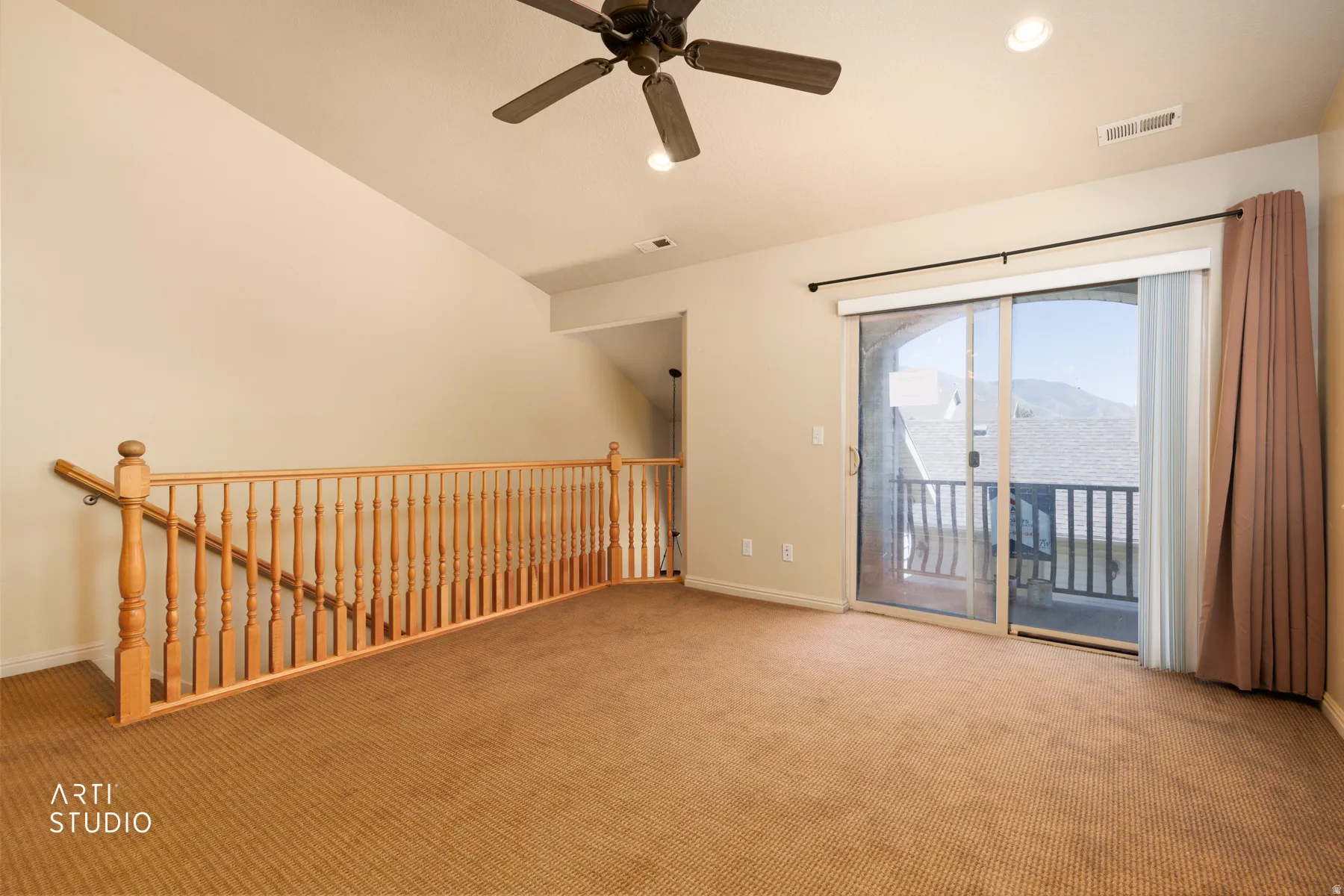 Spacious carpeted loft featuring a vaulted ceiling with a ceiling fan, recessed lighting, natural wood railing, and a sliding glass door opening to a private balcony