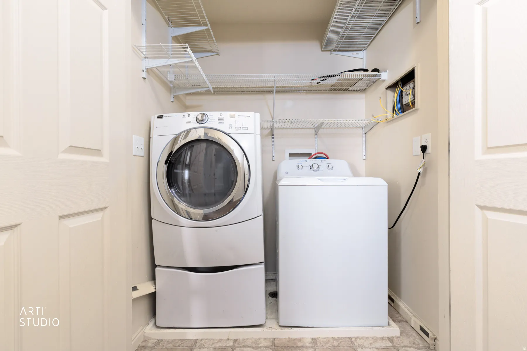 Dedicated laundry area featuring a front-load washer with pedestal, top-load dryer, and multiple wire shelving units for storage
